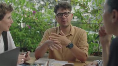 Genç işadamı, çok ırklı iş arkadaşlarıyla planlarını tartışırken açık terasta toplantı yapıyor.