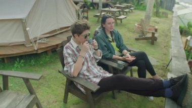 İki genç bayan turistin dışarıda oturup doğa manzarasını tartışırken, dinlenirken ve çay içerken yüksek açılı çekimleri.