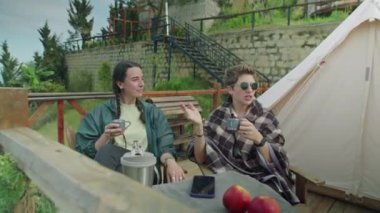 İki genç kadın dışarıda oturmuş çay içiyor ve tatilde dağlarda gezerken manzarayı tartışıyorlar.