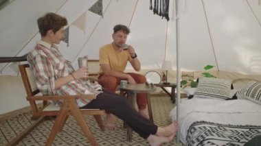 Genç bir adam ve kadının çadırda oturup, çay içip, tatilde konuştuğu bir fotoğraf.