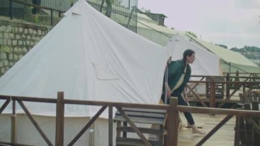 Genç romantik çiftin çadırdan ayrılırken, terasta dikilirken ve tatil yaparken dağ manzarasının keyfini çıkarırken tam yan görüntüsü.