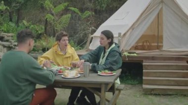 Glampsite 'deki çadırın önünde yemek yerken sohbet eden genç turistlerle dolu orta boy bir çekim.