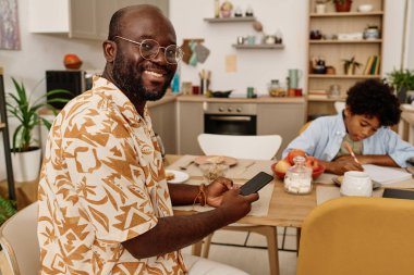 Oğlu ödevini yaparken gülümseyen siyah adam meslektaşlarının mesajlarına cevap veriyor.