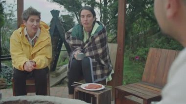 Kamp ateşinin yanında oturan ve arkadaşlarıyla sohbet eden iki genç kadının omuz üstü fotoğrafı doğada dinlenirken ve yemek hazırlarken.