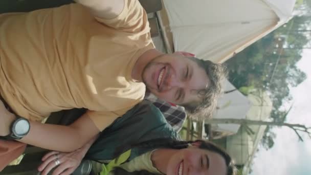 グランピングテントの外に座っている若い喜びのカップルの垂直Pov 自然の夏休みにビデオ通話しながらカメラやチャットを見る — ストック動画