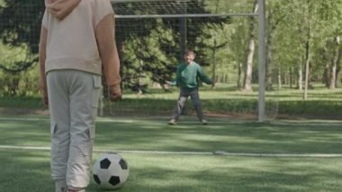 Yavaş çekim, küçük kız futbol topunu tekmeliyor ve çocuk dışarıda parkta oynarken gol kurtarıyor.