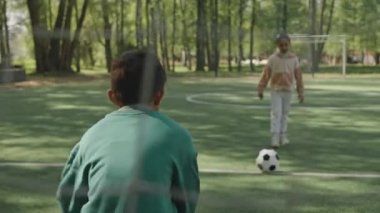 Parkta Asyalı oğlanla futbol oynarken küçük bir kızın kaleye vuruşunu ve heyecanla el çırpışını izle.