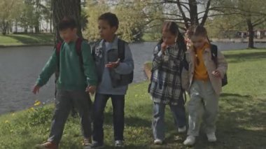 Yaz günü parkta yürüyüp okuldan sonra sohbet eden çoklu etnik kökenli küçük kız ve erkeklerin tam karesi.