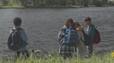 Okul çıkışı birlikte yürürken parkta durup ördeğin gölette yüzüşünü izleyen bir grup çocuk.