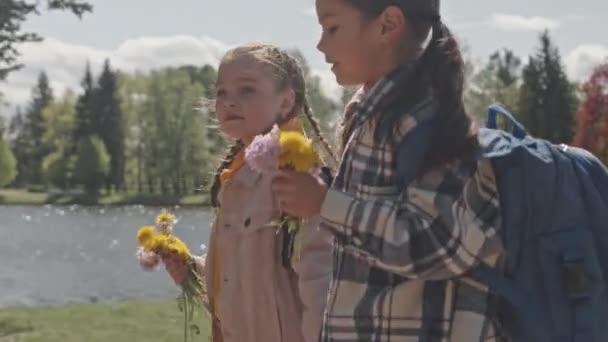 Közepes Felvétel Két Kisiskolás Lányról Hátizsákkal Akik Kéz Kézben Vadvirággal — Stock videók