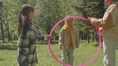 Neşeli küçük kız, yaz günü dışarıda oynarken arkadaşlarının tuttuğu hula çemberinden atlıyor.