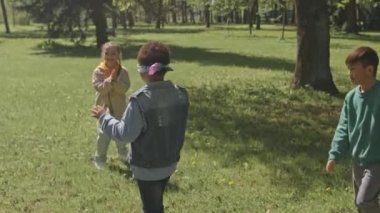 Bir grup küçük kız ve oğlanın parktaki yeşil çimlerde heyecan içinde kör adam oyunu oynamalarının yüksek açılı çekimi.
