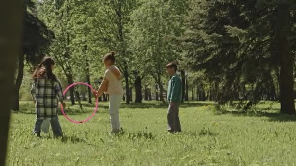 公園の緑の芝生で遊んでいる間フラフープを飛び跳ねる小さな子供のワイドショット — ストック動画