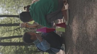Küçük kız ve oğlanların parkta oturup plastik külahları üst üste dizerken çekilmiş dikey görüntüleri.