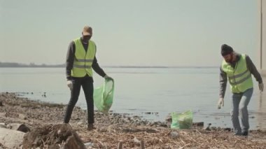 Çevreci gönüllülerin çöpleri toplayıp çöp poşetlerine atarak sahil şeridi temizliği yaptığı tam bir çekim.