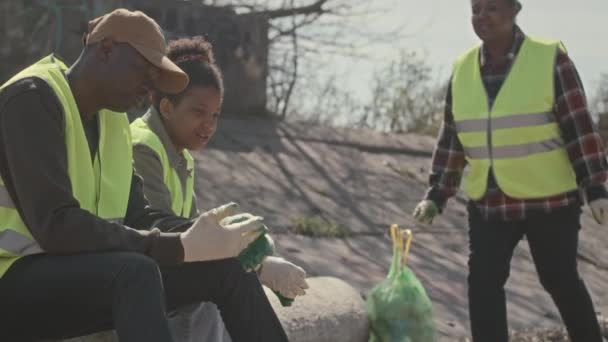 海岸に座っている黒人環境ボランティアのグループ ゴミを収集した後に休んでいる間 笑顔とチャット — ストック動画