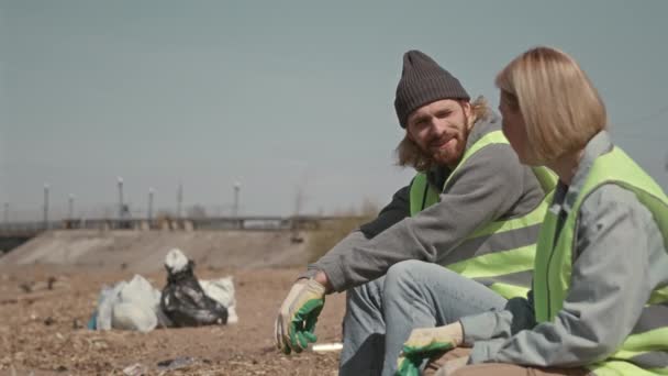 海岸に座っている男性と女性の環境ボランティア ゴミを集めて休憩しながら話す — ストック動画