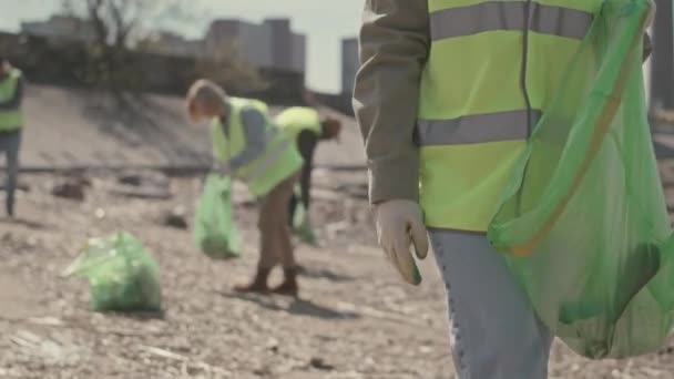 身穿绿色霓虹灯背心 戴着手套的非洲裔美国女孩在与一群环保志愿者一起进行海岸清理的同时 将垃圾收集到垃圾袋中的偷拍照片 — 图库视频影像