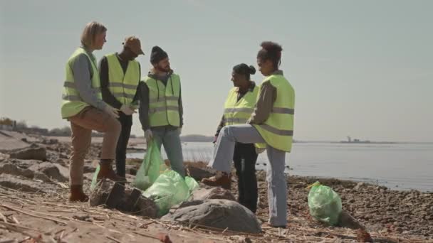海岸にゴミ袋を持って立っている多様な環境活動家のグループのフルショットとゴミ収集中に休憩中に議論 — ストック動画