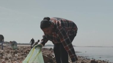 Bir grup çevreci eylemciyle sahil şeridini temizlerken Afrikalı Amerikalı bir kadının çöp poşetine çöp attığı görüntüleri.