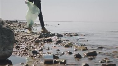 Genç Afrikalı Amerikalı eldiven giyen çevreci plastik şişe ve atıkları çöp poşetlerine toplarken kaldırım taşlarını temizliyor.