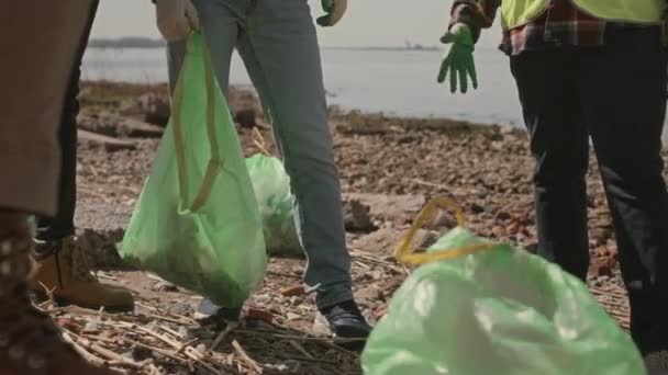 海岸のゴミ袋の周りに立っている環境活動家のグループのクロップショットとゴミ拾いの後に休んでいる間の議論 — ストック動画