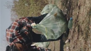 Orman temizliği yaparken çöp torbalarına plastik atık toplayan eldivenli kadın gönüllülerin tam dikey görüntüsü.