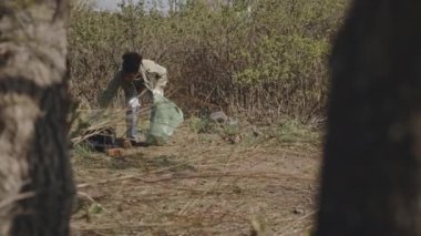 Bir grup çevreci eylemciyle orman temizliği yaparken plastik atık toplayan genç siyah kız ağacının arkasından görüntüyü izle