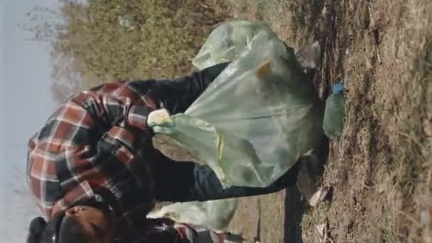 森林清掃中にプラスチックごみをゴミ袋に収集する手袋の女性環境ボランティアの垂直フルショット — ストック動画