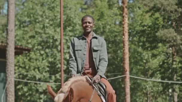 年轻的黑人骑着马 高高兴兴地坐在田边的马鞍上拍照 — 图库视频影像