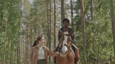 Binicilik okulundaki derste bayan eğitmenin yardımıyla gülümseyen siyah adamın düşük açılı görüntüsü.