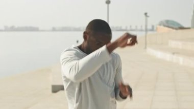 Şehir dışında, nehir kenarında gölgelerde boks yaparken Afrika kökenli Amerikalı sporcunun havaya yumruk attığı orta boy bir fotoğraf.