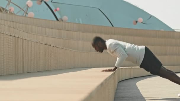 スポーツウェアの強い黒人男性は 朝のトレーニング中に都市の公共スペースでプッシュアップをクラッピング — ストック動画