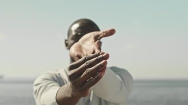 Yazın dışarıda egzersiz yaparken bileklerini kameranın önünde esneten siyah erkek sporcunun görüntüsü.