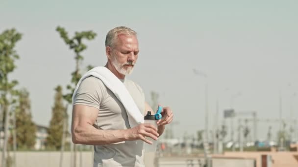 早晨外出锻炼后 身穿运动服的老年男子一边喝酒 一边用毛巾擦拭额头 — 图库视频影像