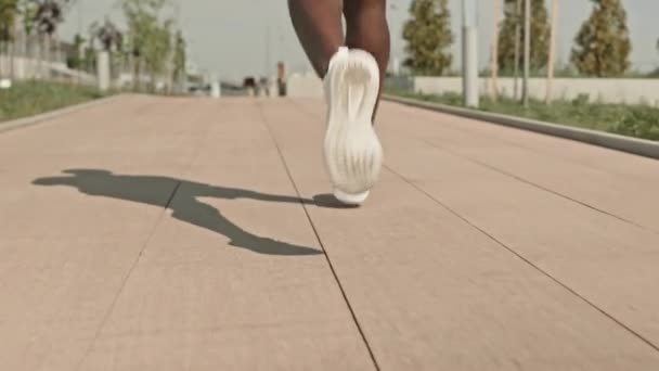 低いセクション 夏の日に市街地でジョギングする認識できない黒人スポーツマンの脚のスローモーションショット — ストック動画