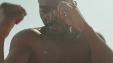 Gündüz vakti dışarıda boks yaparken kaslı gövdesiyle yumruk antrenmanı yapan üstsüz Afrikalı Amerikalı adamın orta yavaş çekim çekimi.