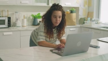 Orta boy kıvırcık saçlı bir kızın evde online alışveriş yaparken dizüstü bilgisayar ve kredi kartı kullandığı bir fotoğraf.