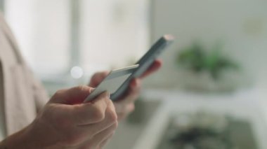 Cep telefonu uygulaması ile online alışveriş yaparken elinde kredi kartı tutan ve bilgilerini akıllı telefondan yazan adamın yakın çekim görüntüleri.