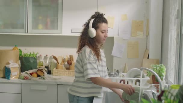 Νεαρή Κοπέλα Ασύρματα Ακουστικά Πλένει Πιάτα Χορεύει Και Απολαμβάνει Μουσική — Αρχείο Βίντεο