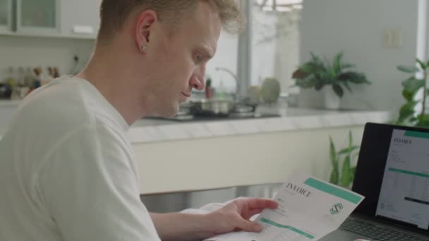 Junger Mann Benutzt Taschenrechner Schaut Sich Ausgedruckte Rechnungen Und Bezahlt — Stockvideo