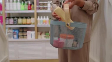 Elinde alışveriş sepeti olan bir kadının kozmetik ürünlerini ödemek için kasiyere gitmesi.