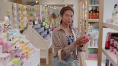 Markette alışveriş yaparken elinde krem tutan siyah, neşeli kadın portresi. Kameraya bakıyor.