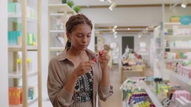 Kozmetik dükkanından güzellik ürünleri alırken orta boy siyah bir kadının ruj seçtiği bir fotoğraf.