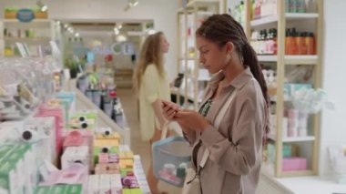 Yüz maskesi arayan kadın müşterinin yan görüntüsü mağazada kozmetik ürünlerle dolu rafın yanında duran cilt tipine göre