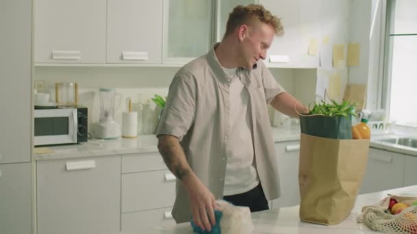 Young Man Unloading Groceries Paper Bag Talking Mobile Phone Kitchen — Stock Video