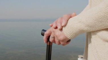 Yaşlı bir kadının göl rıhtımında ayakta dikilirken bastona yaslandığı yakın çekim.
