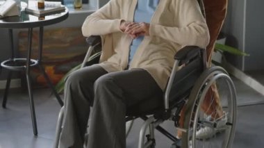 Tekerlekli sandalyedeki yaşlı kadınla yürüyen ve konuşan kadın sosyal hizmetler görevlisinin fotoğrafını çek.