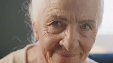 Kameraya bakan gri saçlı ve yüzü kırışık yaşlı bir kadının yakın portresi.