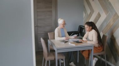 Kadın sosyal hizmet görevlisi ve üst düzey bir kadının faturaları kontrol ederken ve kişisel finansmanı birlikte yönetirken yüksek açılı görüntüsü.